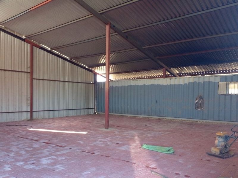 A large, open-plan utility or storage space featuring corrugated metal walls, a high metal roof, and durable paved flooring.
