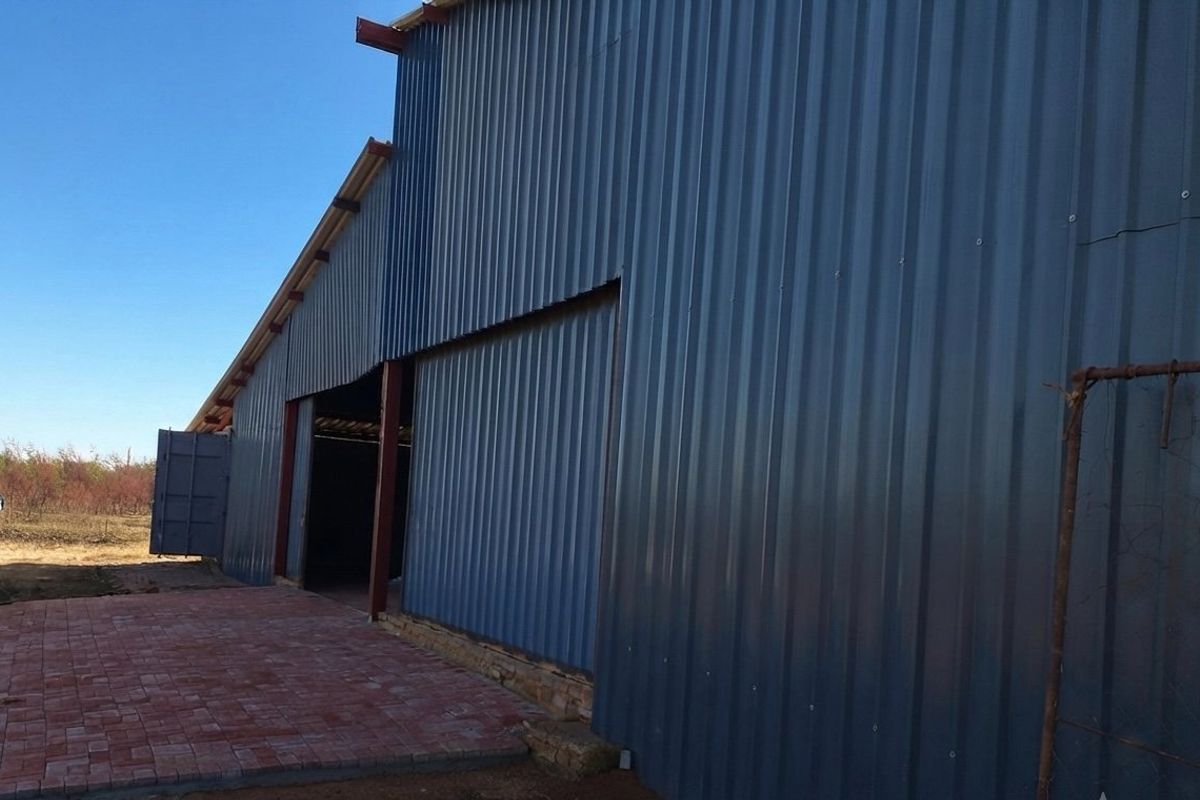 Exterior view of a large farm shed featuring corrugated metal cladding, a steel frame, and a paved entrance area.