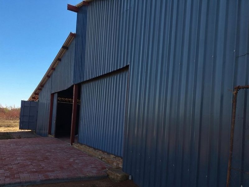 Exterior view of a large farm shed featuring corrugated metal cladding, a steel frame, and a paved entrance area.