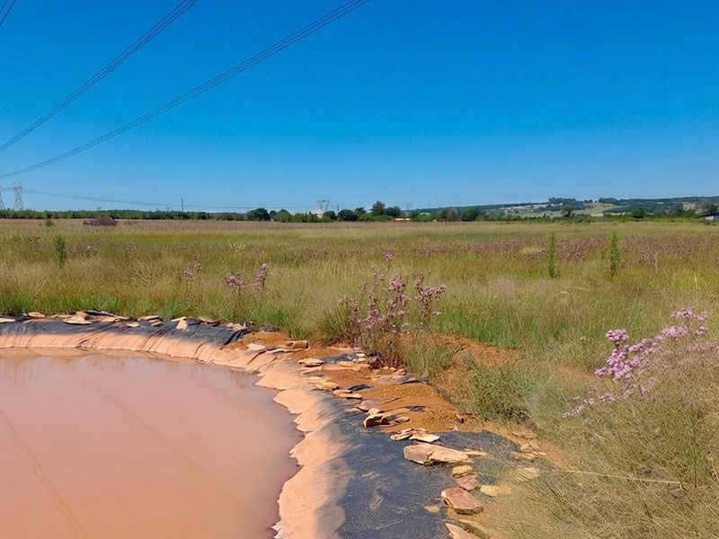 A wide view of the farm landscape featuring an earthen dam with exposed liner and overhead power lines crossing the open field.