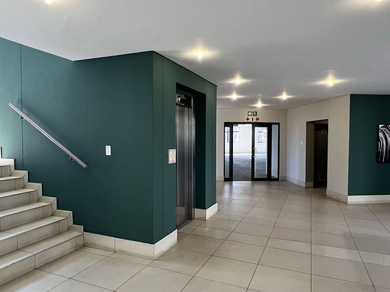 A modern, well-maintained commercial building lobby featuring tiled flooring, a central elevator, and a staircase with a stainless steel handrail.