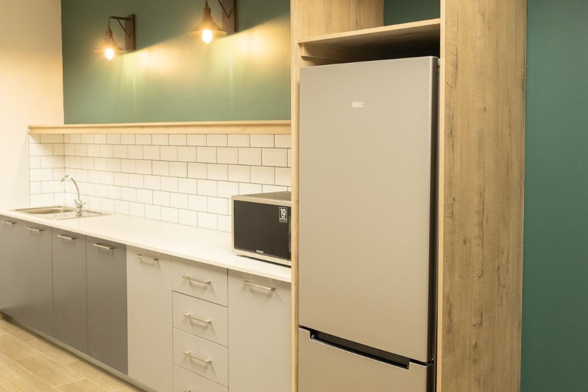 Modern commercial kitchenette featuring sleek cabinetry, subway tile backsplash, integrated refrigerator housing, and stylish wall-mounted lighting.