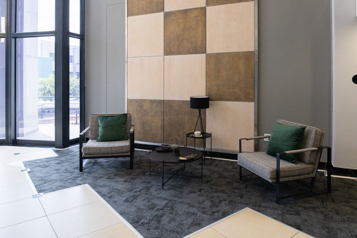 A modern commercial lounge area featuring a decorative feature wall, large floor-to-ceiling windows, and a combination of carpeted and tiled flooring.