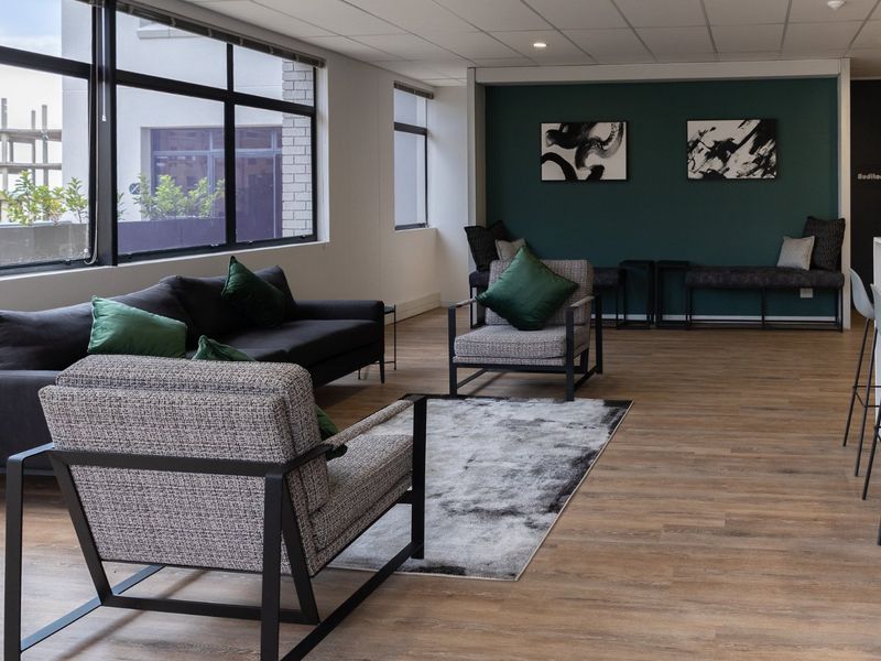 A modern open-plan commercial lounge area featuring laminate wood flooring, large windows for natural light, and built-in bench seating against a feature wall.