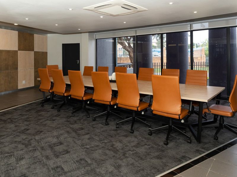 A modern, well-lit commercial boardroom featuring a large conference table, wood paneling, and expansive windows overlooking the exterior.