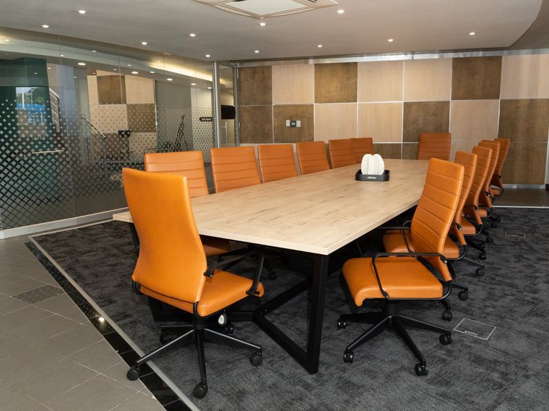 A modern, professional boardroom featuring a large conference table, glass partitioning, and contemporary wall paneling with recessed ceiling lighting.