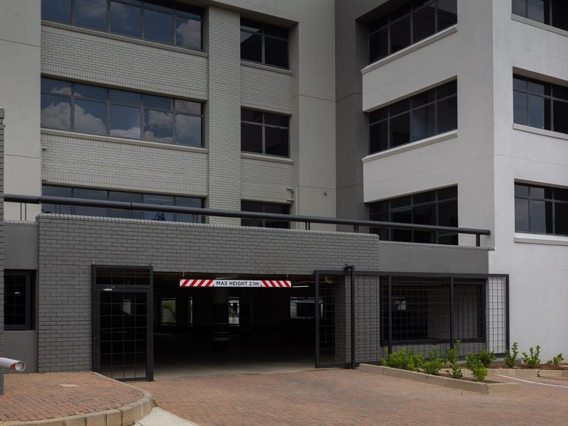 Commercial building exterior featuring a secure parking garage entrance with height restriction signage, modern brick facade, and paved driveway access.