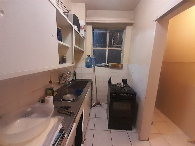 A compact kitchen featuring built-in cabinetry, a stainless steel sink, and a freestanding stove, with tiled splashbacks and flooring throughout.