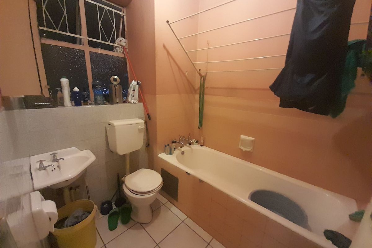 A functional bathroom featuring a bathtub, pedestal basin, and toilet, with tiled flooring and a wall-mounted drying rack.