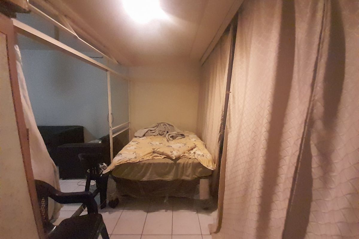 A bedroom space featuring tiled flooring and a sliding room divider, currently showing signs of wear and poor lighting conditions.