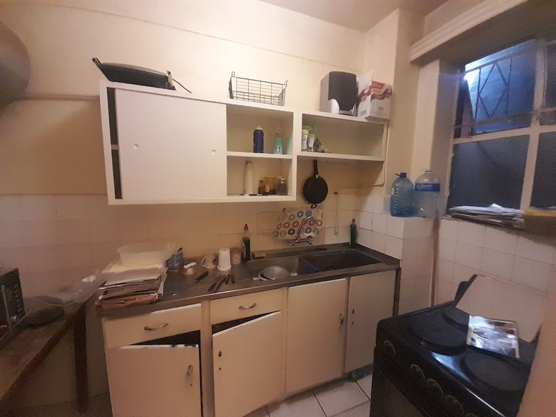 A dated kitchen featuring a stainless steel sink, tiled backsplash, and original cabinetry in need of renovation and modernization.