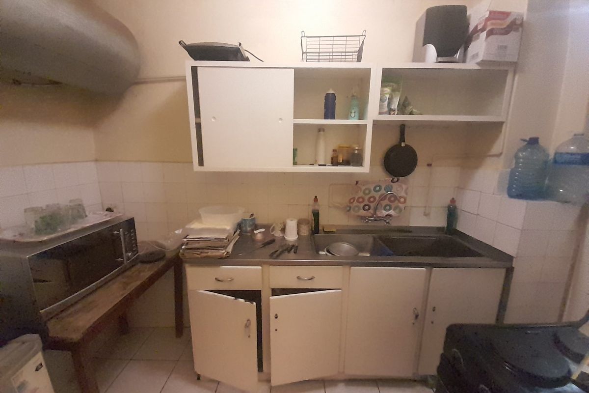 A functional kitchen area featuring tiled splashbacks, stainless steel sink, and built-in cabinetry, currently showing signs of wear and requiring cosmetic updates.