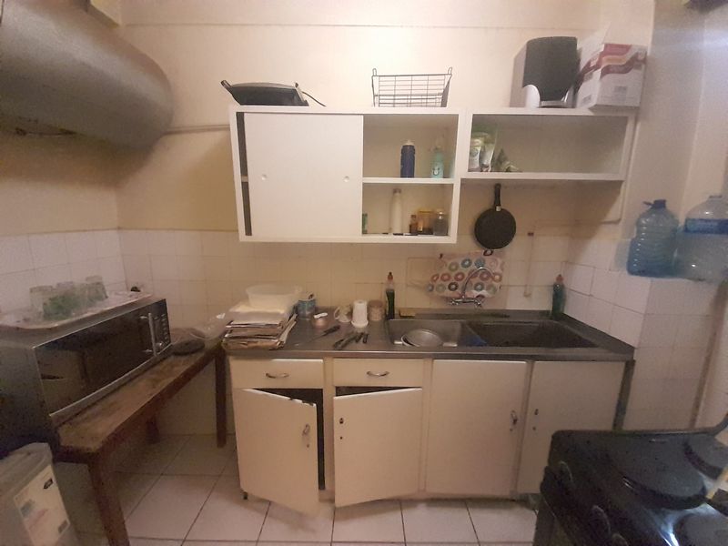 A functional kitchen area featuring tiled splashbacks, stainless steel sink, and built-in cabinetry, currently showing signs of wear and requiring cosmetic updates.