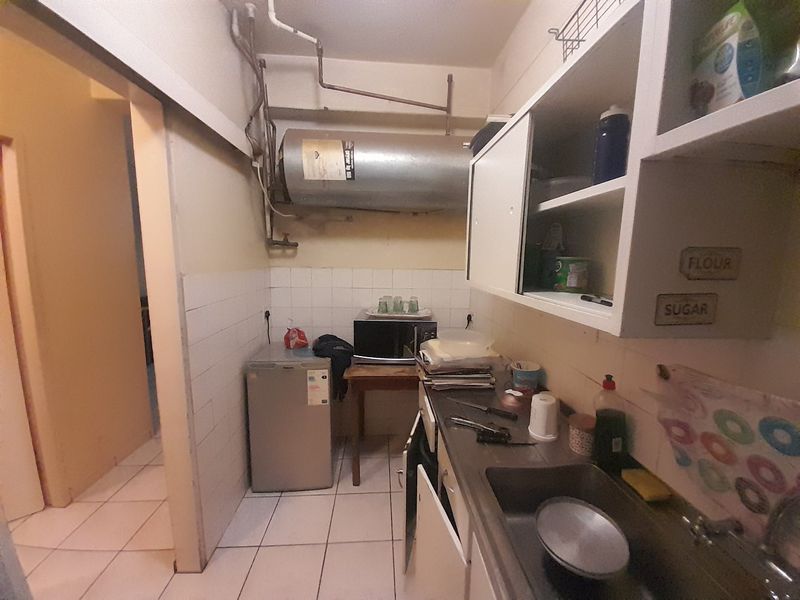 A functional scullery area featuring built-in cabinetry, a stainless steel sink, tiled splashbacks, and exposed utility infrastructure.