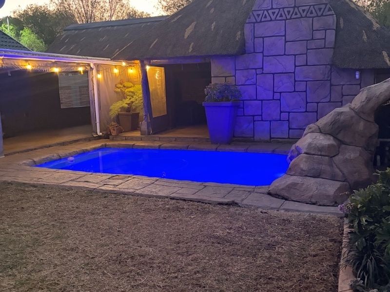 Outdoor entertainment area featuring a swimming pool, rock feature, and a thatched-roof structure with stone cladding.