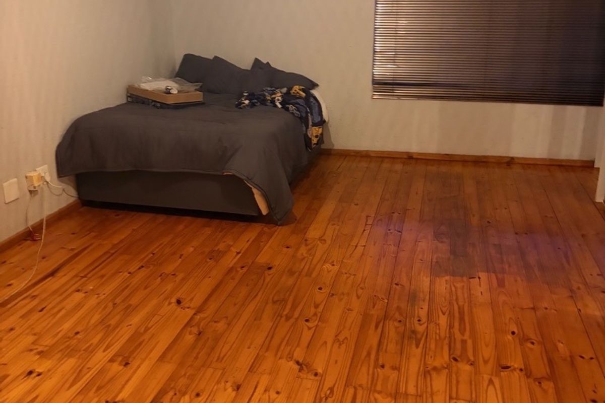 Spacious bedroom featuring polished timber flooring, a wall-mounted split-system air conditioner, and venetian blinds.