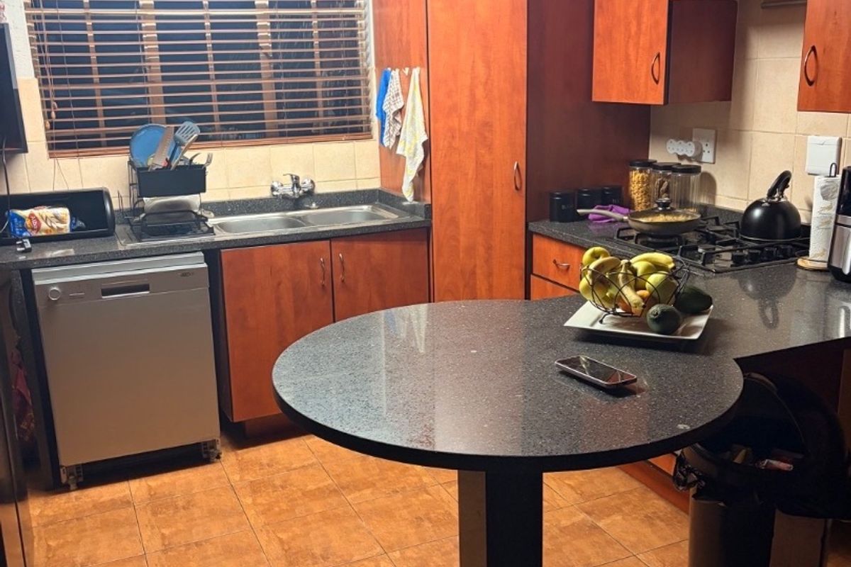 A functional kitchen featuring wood-finish cabinetry, granite countertops, a gas hob, and a built-in breakfast nook, with tiled flooring throughout.
