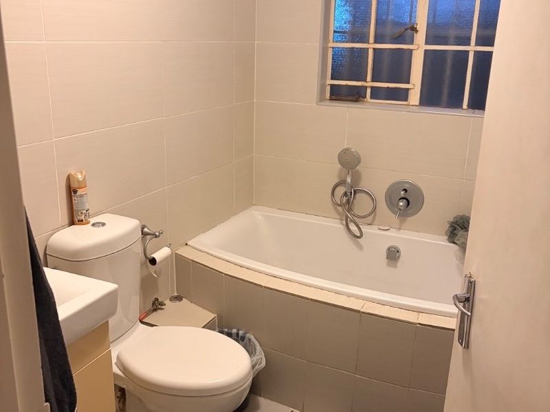 A functional bathroom featuring a built-in bathtub with handheld shower, toilet, and vanity basin, finished with neutral wall and floor tiles.