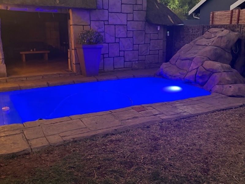 Outdoor pool area featuring a swimming pool with a rock feature, stone chimney, and a thatched roof structure.