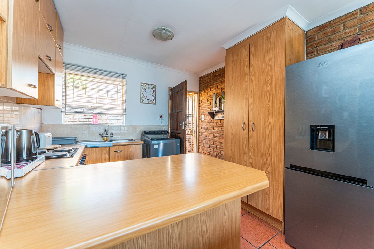 Functional kitchen featuring laminate cabinetry, exposed brick wall accents, tiled flooring, and a practical layout with ample storage and counter space.