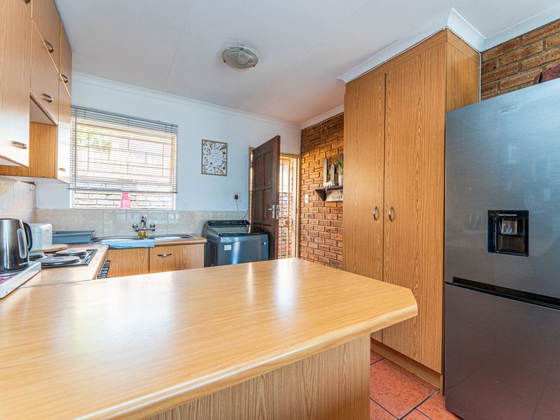 Functional kitchen featuring laminate cabinetry, exposed brick wall accents, tiled flooring, and a practical layout with ample storage and counter space.