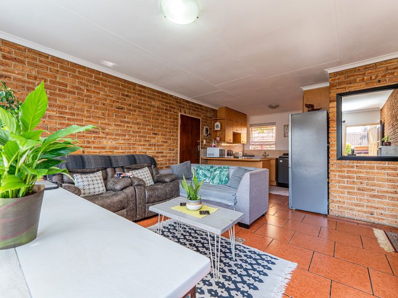 Open-plan living area featuring exposed brick walls and ceramic tile flooring, seamlessly connecting to a functional kitchen space.
