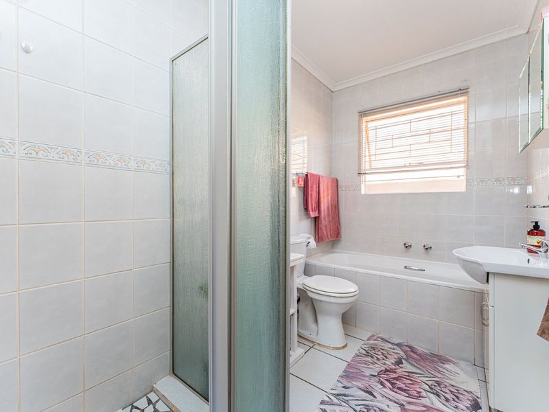 A functional bathroom featuring a shower enclosure, bathtub, toilet, and vanity basin with neutral wall and floor tiling.