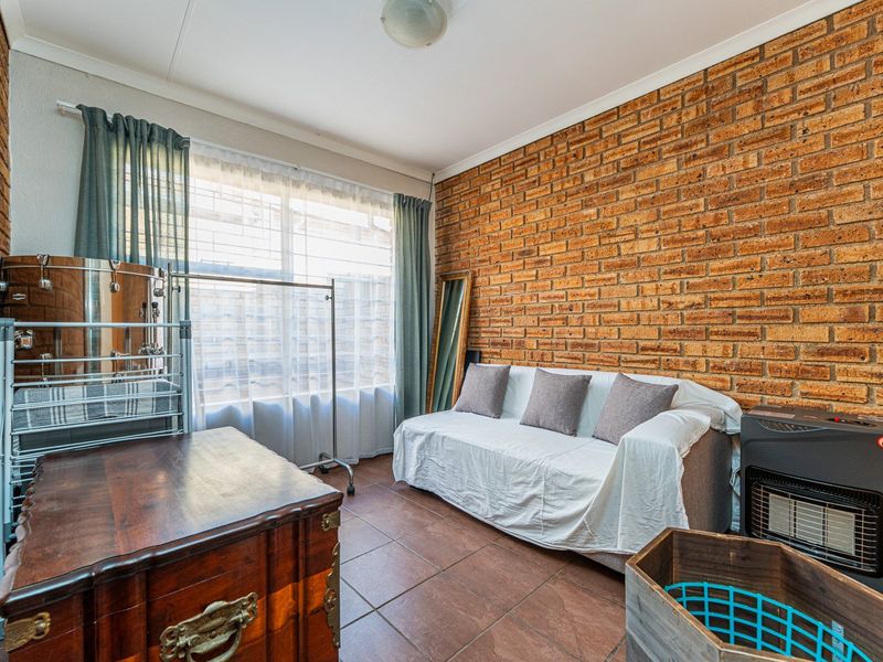 Living room featuring exposed brick walls, tiled flooring, and a large window providing natural light.