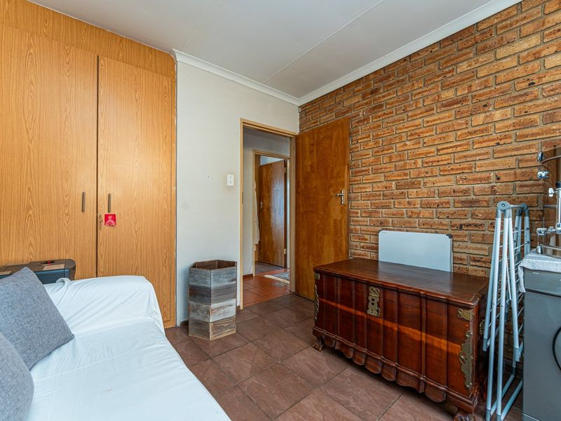 Bedroom featuring exposed brick wall, built-in wooden cupboards, and tiled flooring, offering a functional space with potential for modern updates.