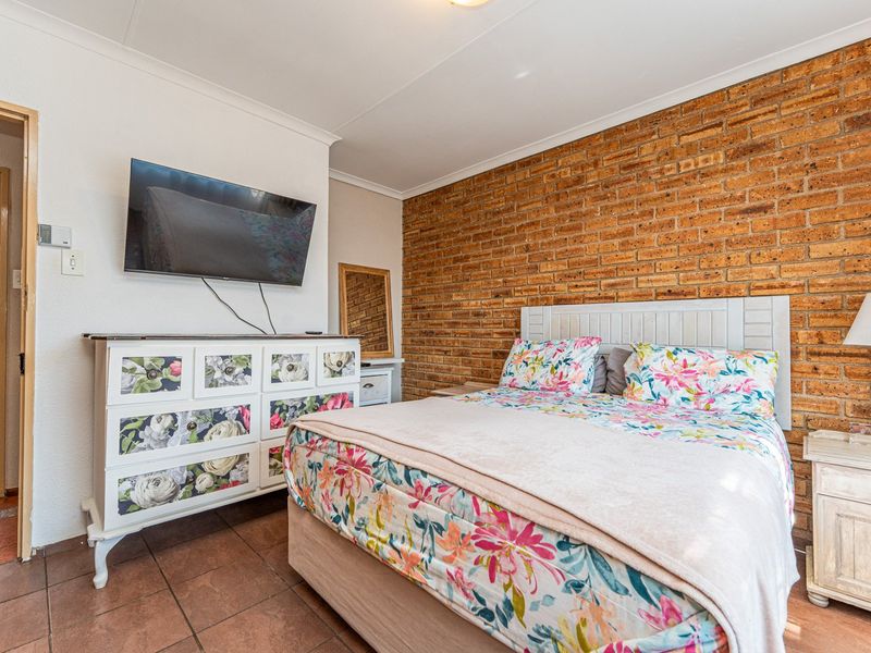A bedroom featuring an exposed brick accent wall, tiled flooring, and coved ceiling, with direct access to an adjoining bathroom.