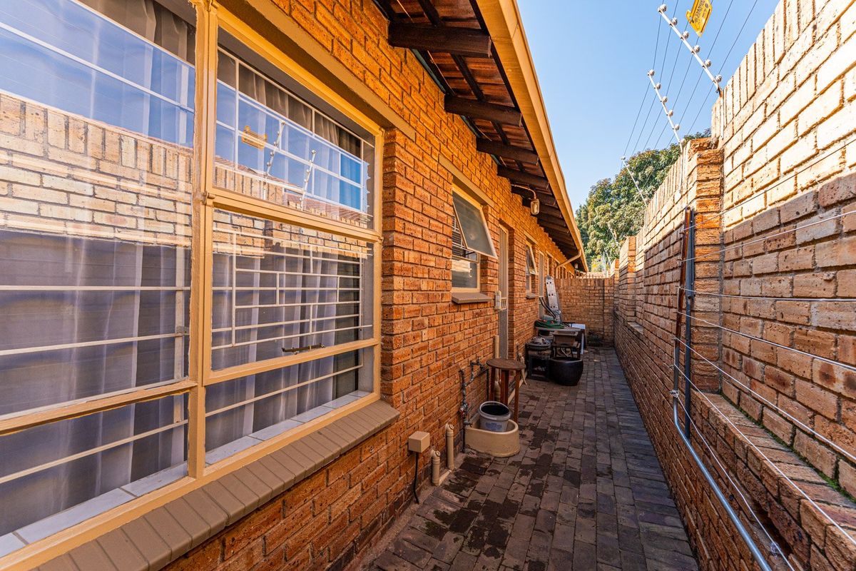 A side exterior walkway featuring face brick walls, paved flooring, and security measures including window bars and electric fencing.