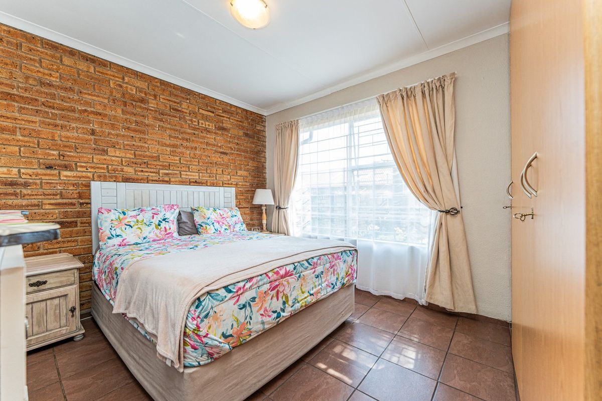 A cozy bedroom featuring an exposed brick accent wall, tiled flooring, and built-in cupboards, offering a warm and functional living space.