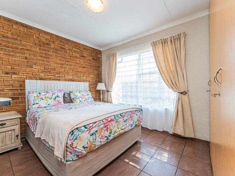 A cozy bedroom featuring an exposed brick accent wall, tiled flooring, and built-in cupboards, offering a warm and functional living space.