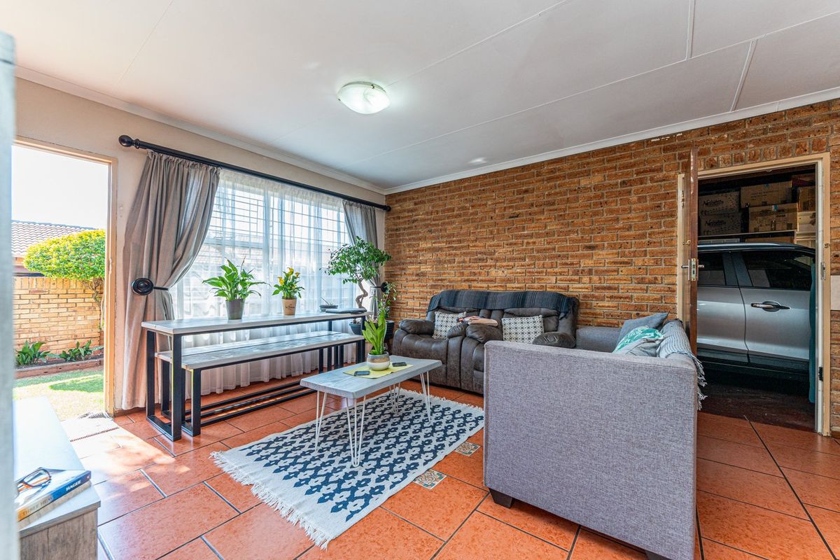 A living room featuring an exposed brick feature wall, terracotta floor tiles, and direct access to an outdoor area through a sliding glass door.