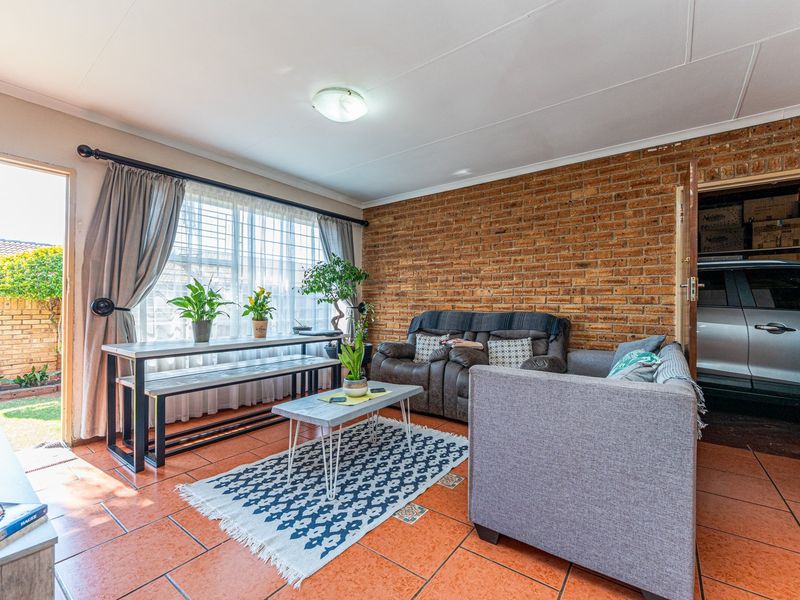 A living room featuring an exposed brick feature wall, terracotta floor tiles, and direct access to an outdoor area through a sliding glass door.