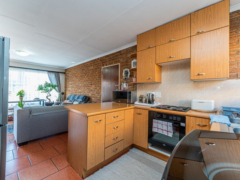 Open-plan kitchen and living area featuring exposed brick walls, wooden cabinetry, and tiled flooring, creating a warm and functional living space.
