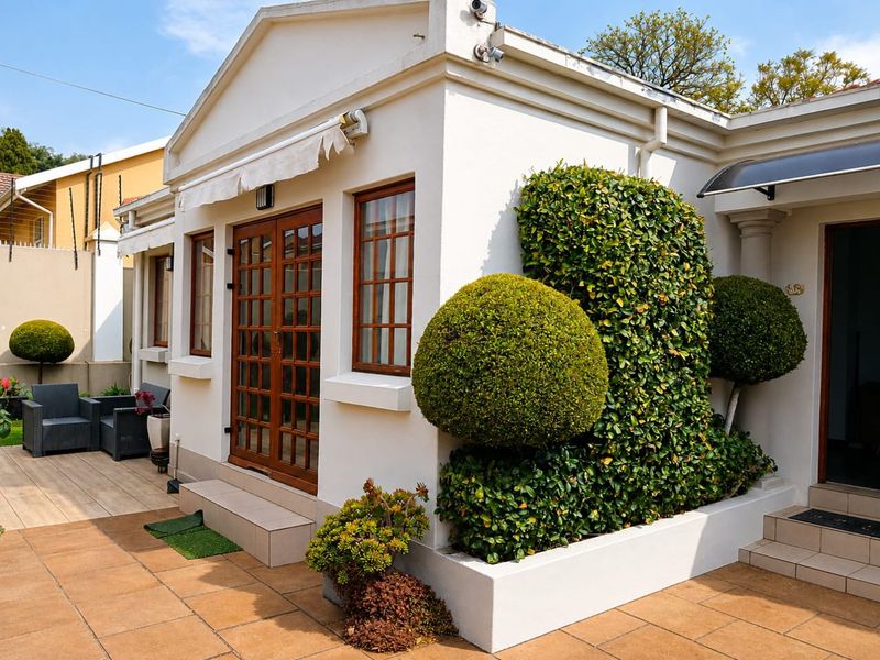 A well-maintained rear exterior featuring a tiled patio, timber-framed glass doors, a retractable awning, and a neatly landscaped raised garden bed.
