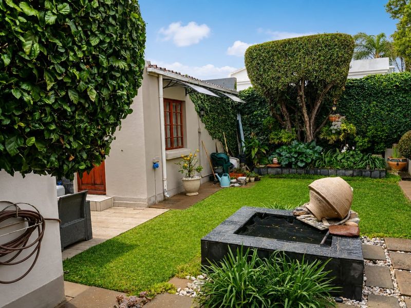 A well-maintained private garden featuring a manicured lawn, established hedges, and a built-in stone water feature with an adjacent paved patio area.