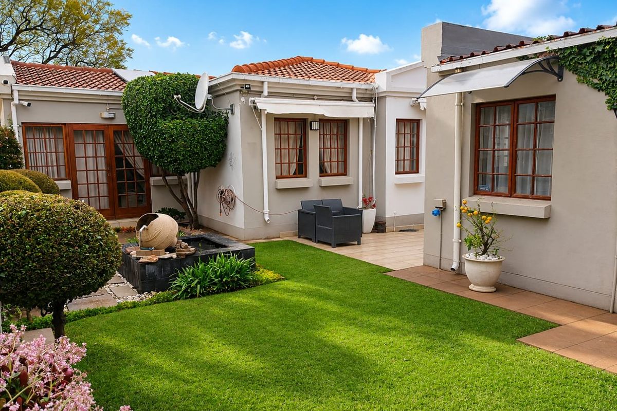 A well-maintained rear garden featuring a manicured lawn, a decorative water feature, and a paved patio area with a retractable awning.