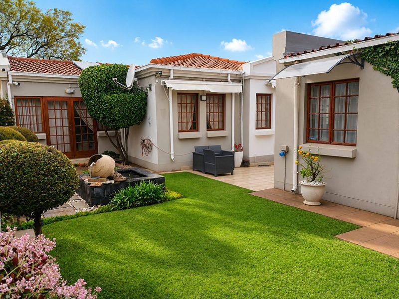A well-maintained rear garden featuring a manicured lawn, a decorative water feature, and a paved patio area with a retractable awning.