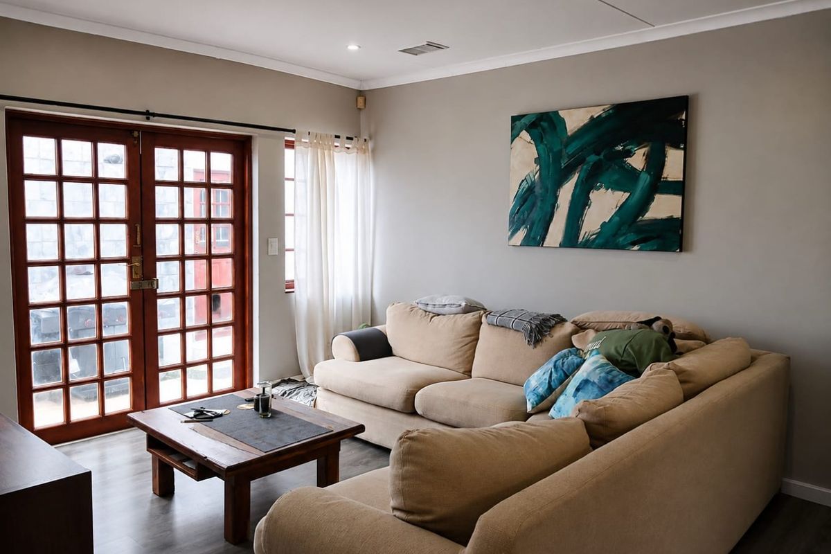 A well-lit living room featuring timber french doors, modern laminate flooring, and recessed downlighting, creating a comfortable and functional space.