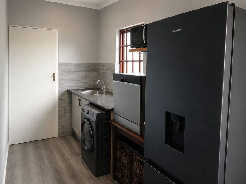 A functional laundry room featuring a stainless steel sink, tiled backsplash, laminate countertops, and modern cabinetry with durable flooring.