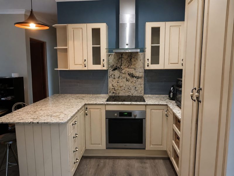 A well-appointed kitchen featuring granite countertops, shaker-style cabinetry, a built-in oven with electric hob, and a stylish subway tile backsplash.