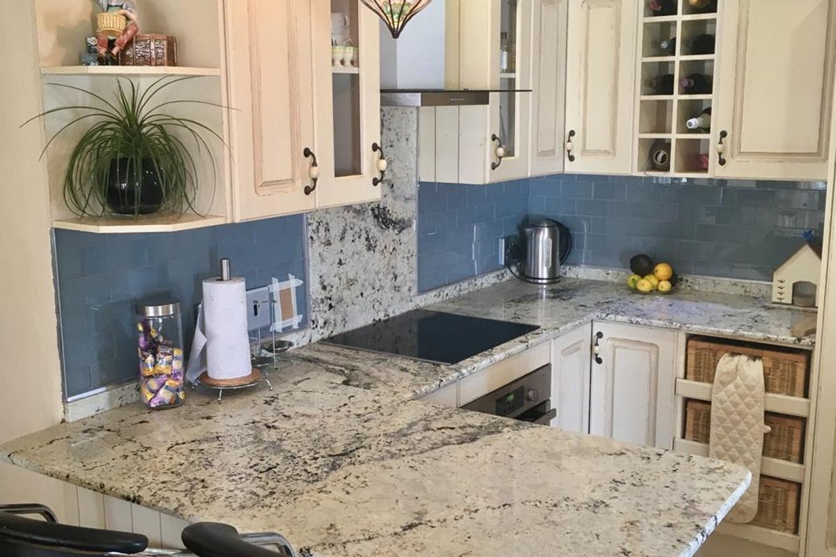 A well-maintained kitchen featuring granite countertops, blue subway tile backsplash, built-in oven, electric cooktop, and integrated cabinetry with a breakfast bar.