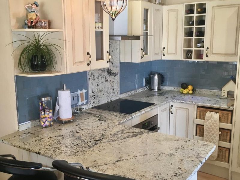 A well-maintained kitchen featuring granite countertops, blue subway tile backsplash, built-in oven, electric cooktop, and integrated cabinetry with a breakfast bar.