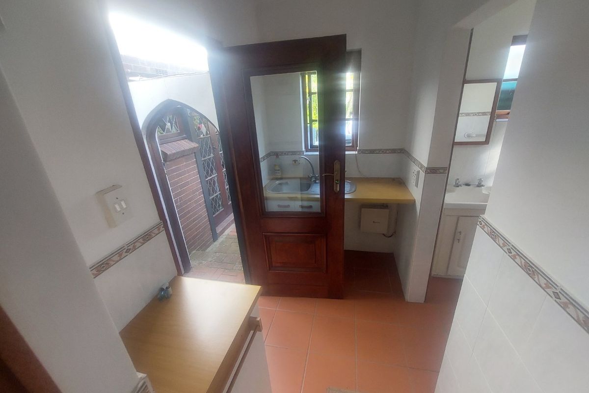 A functional scullery or utility area featuring tiled flooring, a built-in sink, and direct access to an outdoor space.