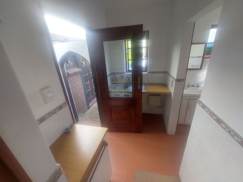 A functional scullery or utility area featuring tiled flooring, a built-in sink, and direct access to an outdoor space.