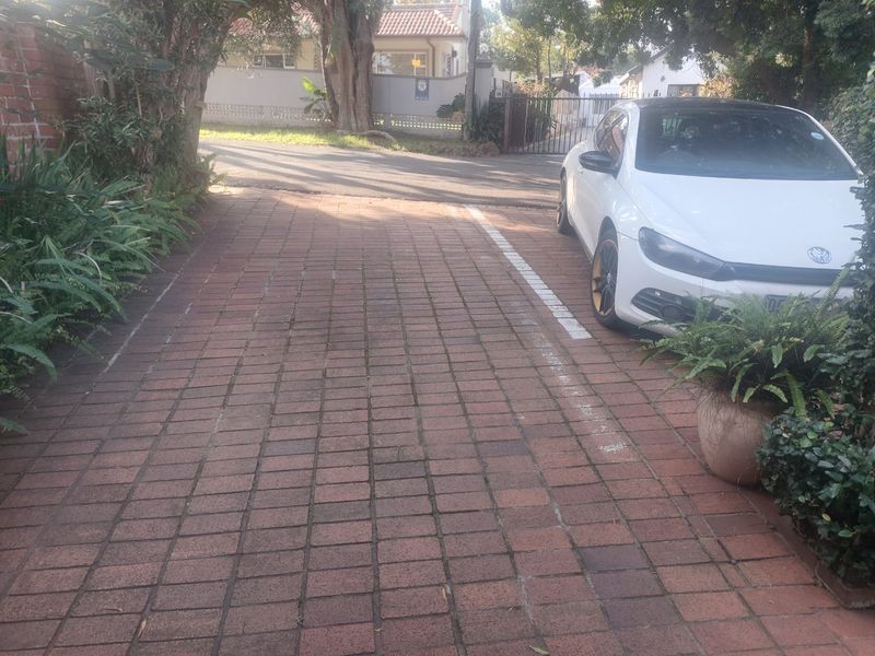 A paved driveway area leading to the property entrance, featuring a brick surface and boundary wall enclosure.