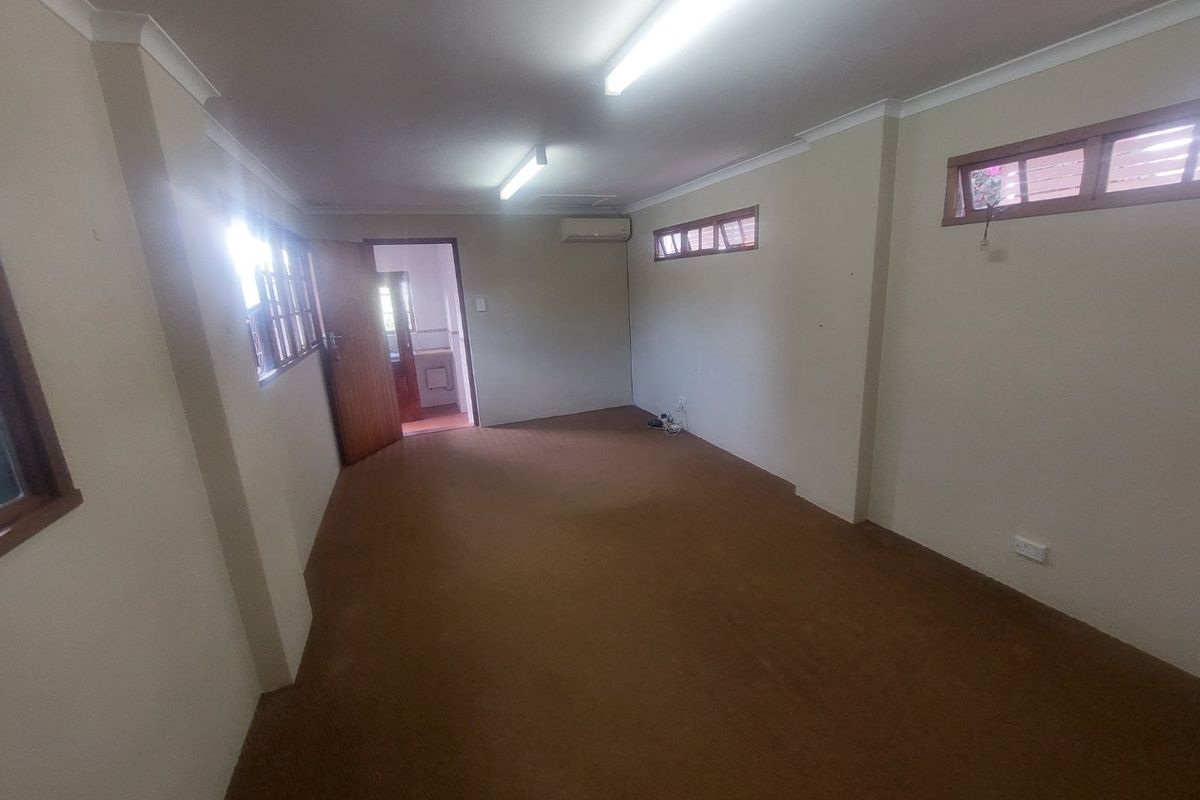 An empty, functional office space featuring carpet flooring, split-system air conditioning, and natural light through timber-framed windows.