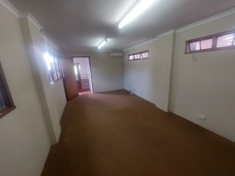 An empty, functional office space featuring carpet flooring, split-system air conditioning, and natural light through timber-framed windows.